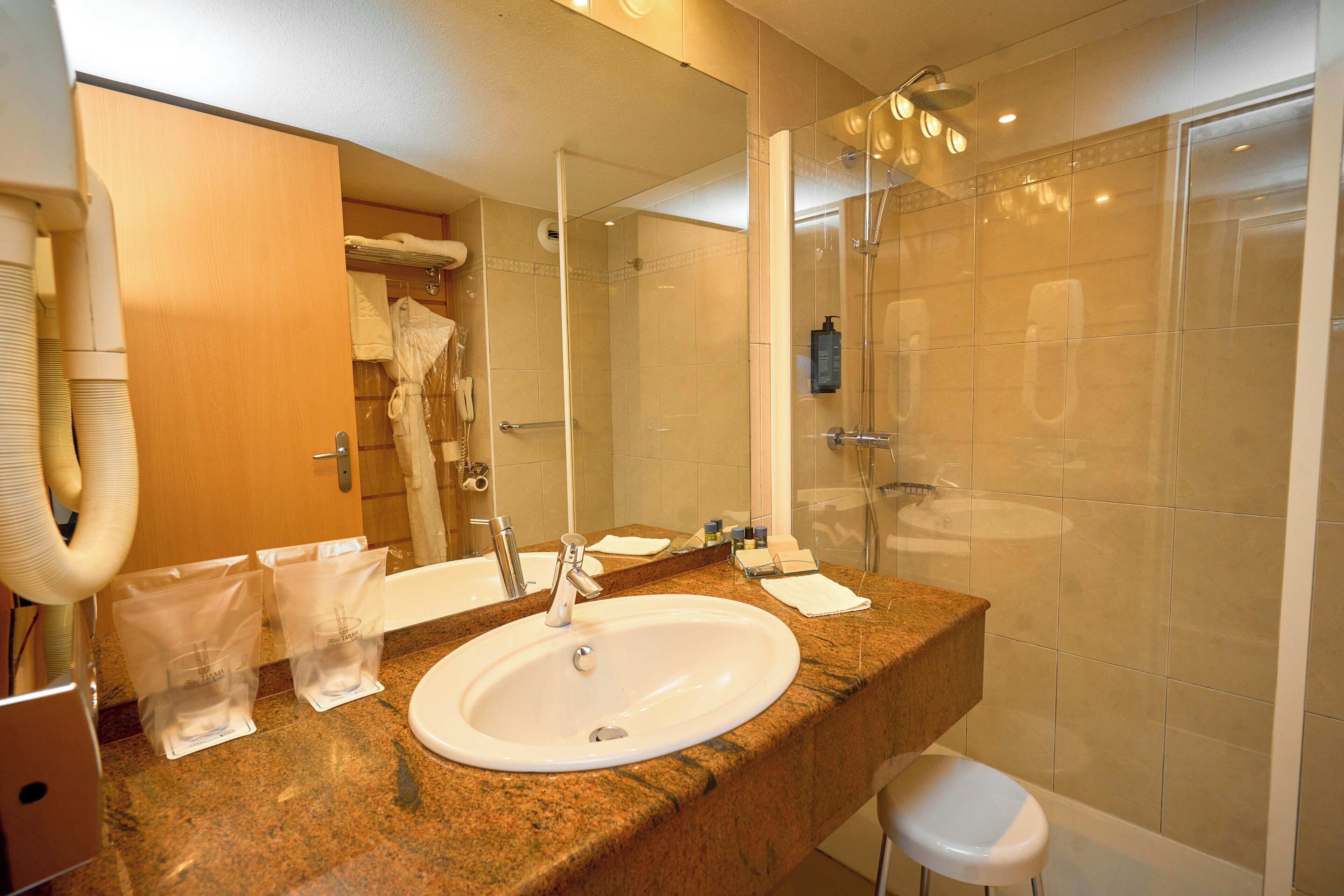 A bathroom with a sink, mirror, shower, and a towel rack.