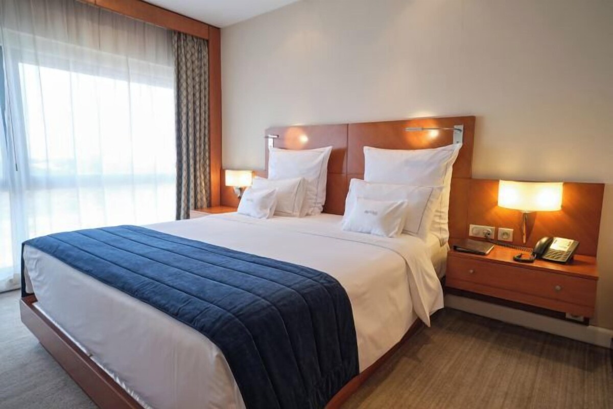 A hotel room with a large bed, two bedside tables with lamps, and a window with curtains.