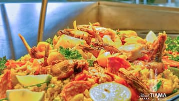 A seafood paella dish with shrimp, chicken, and rice, garnished with lemon slices and parsley.