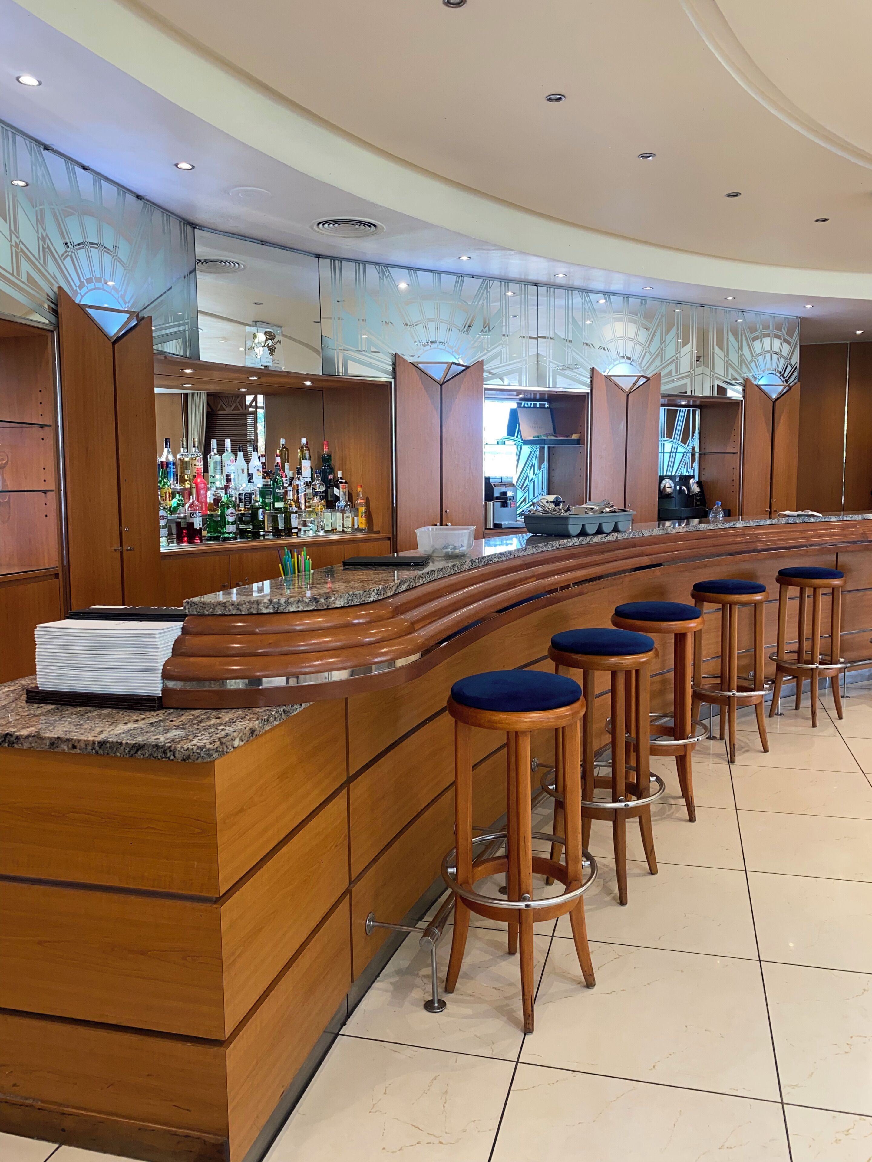 Eine Bar mit einer gebogenen Holztheke, mehreren Sitzhocker und einer Auswahl an Flaschen in Regalen.