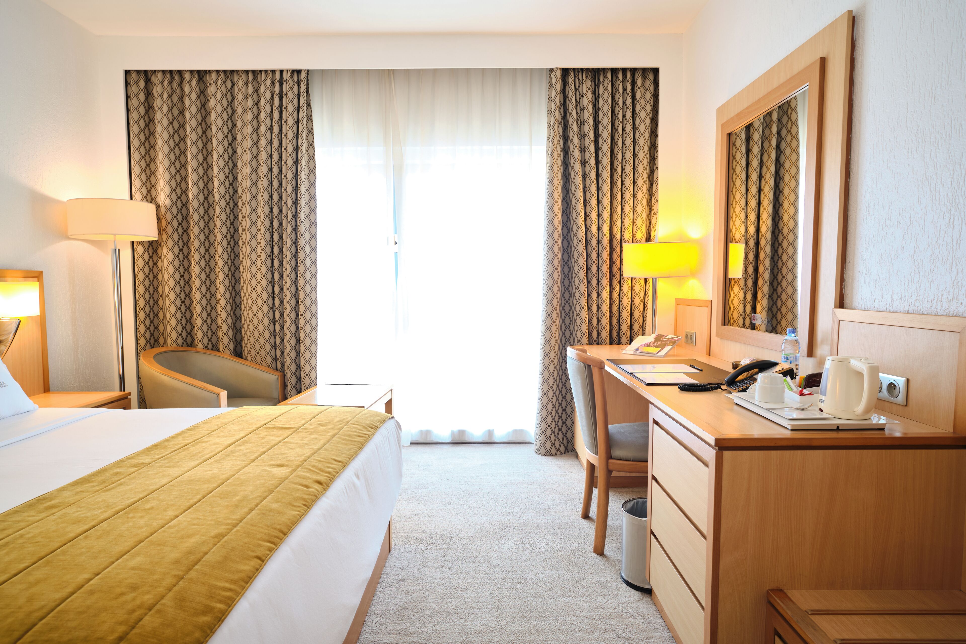 Habitación de hotel con cama, escritorio, silla y un espejo grande.