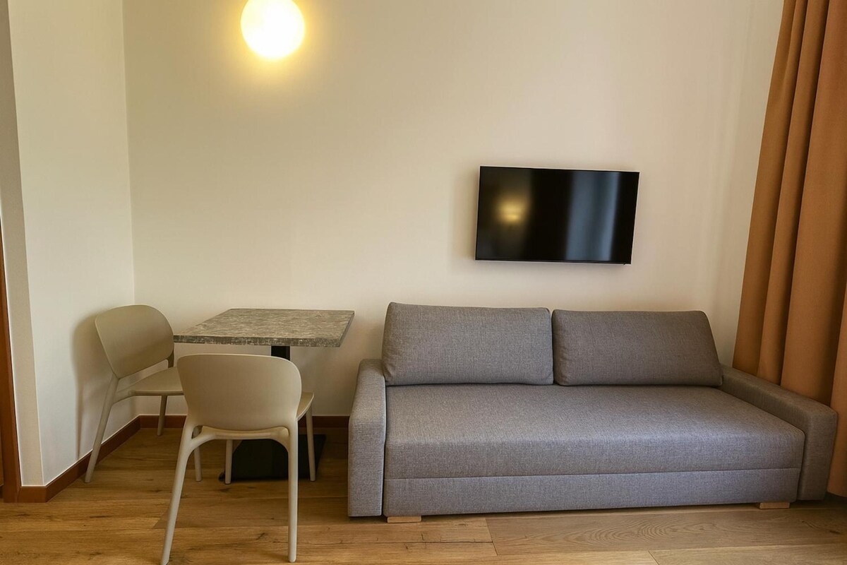 Una sala moderna con un sofá gris, una mesita, una silla y un televisor de pantalla plana montado en la pared.