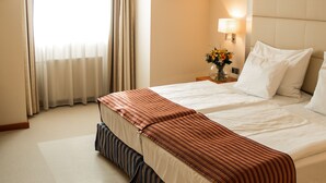 Habitación de hotel con una cama grande, una mesita de noche con lámpara, una ventana con cortinas e iluminación en el techo.