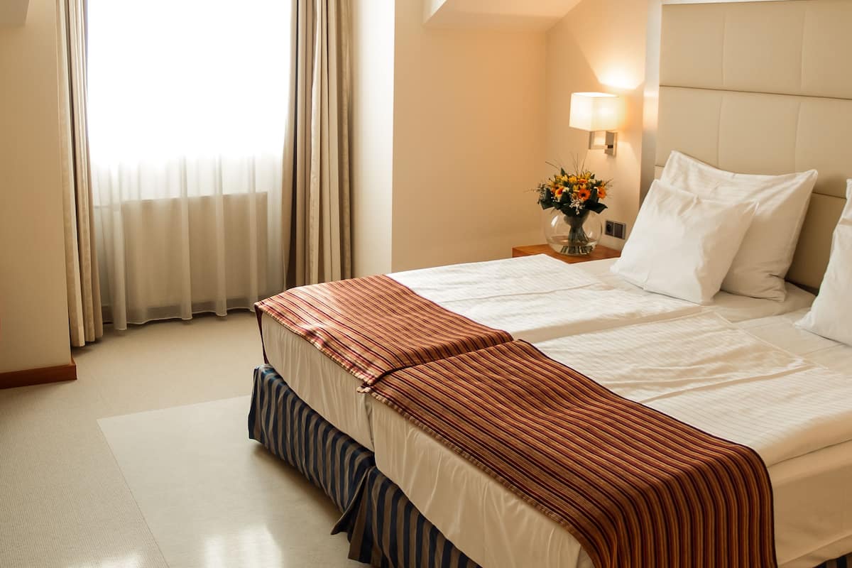 A hotel room with a large bed, a nightstand with a lamp, and a window with curtains.