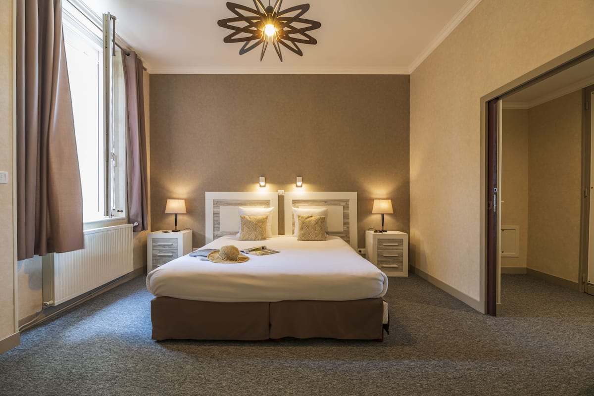 A hotel room with a large bed, two bedside tables with lamps, a radiator, and a modern ceiling light fixture.