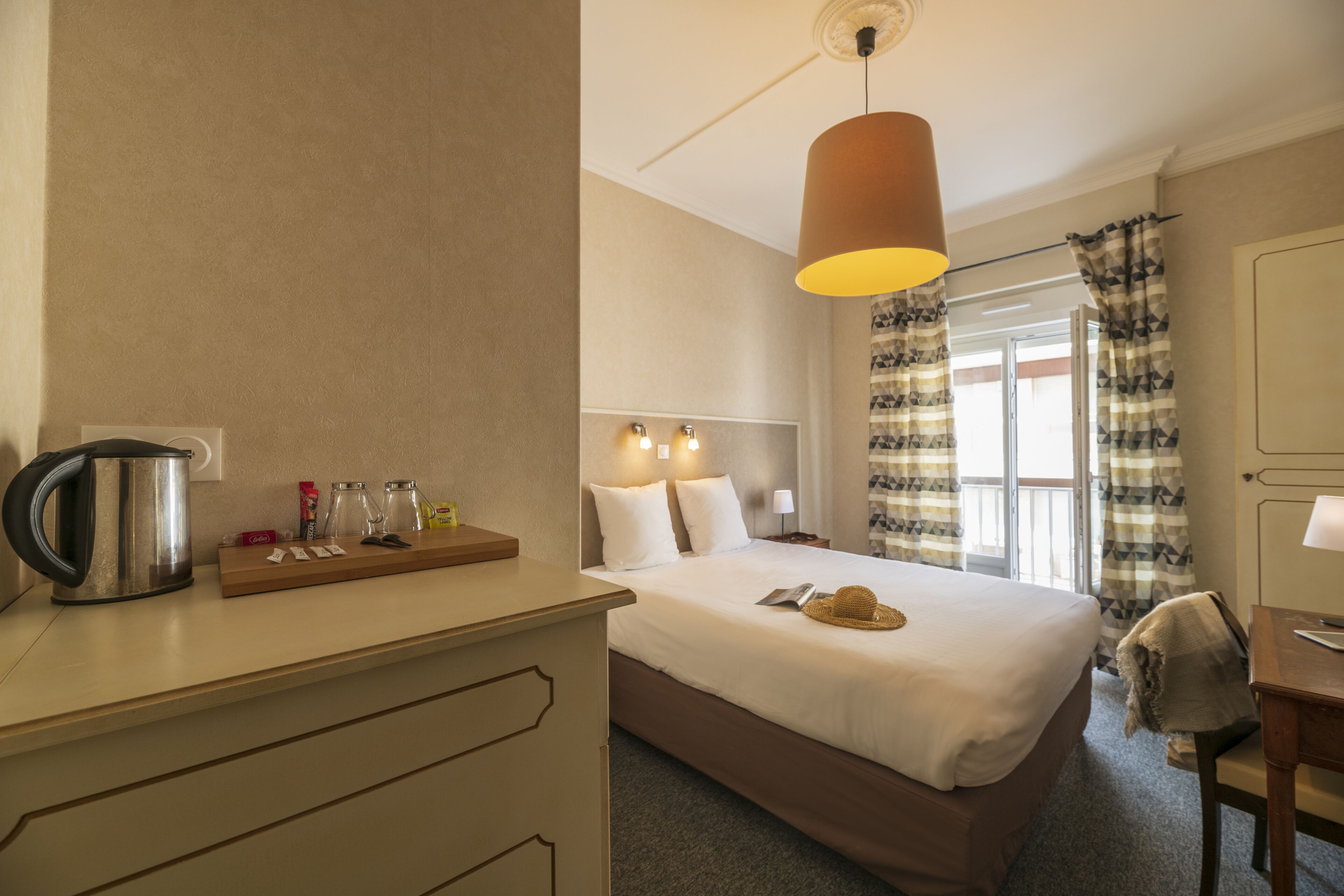 Quarto de hotel com cama, mesa de cabeceira, luminária e vista para o exterior.