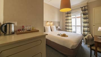Habitación de hotel con cama, mesita de noche, lámpara y vistas al exterior.