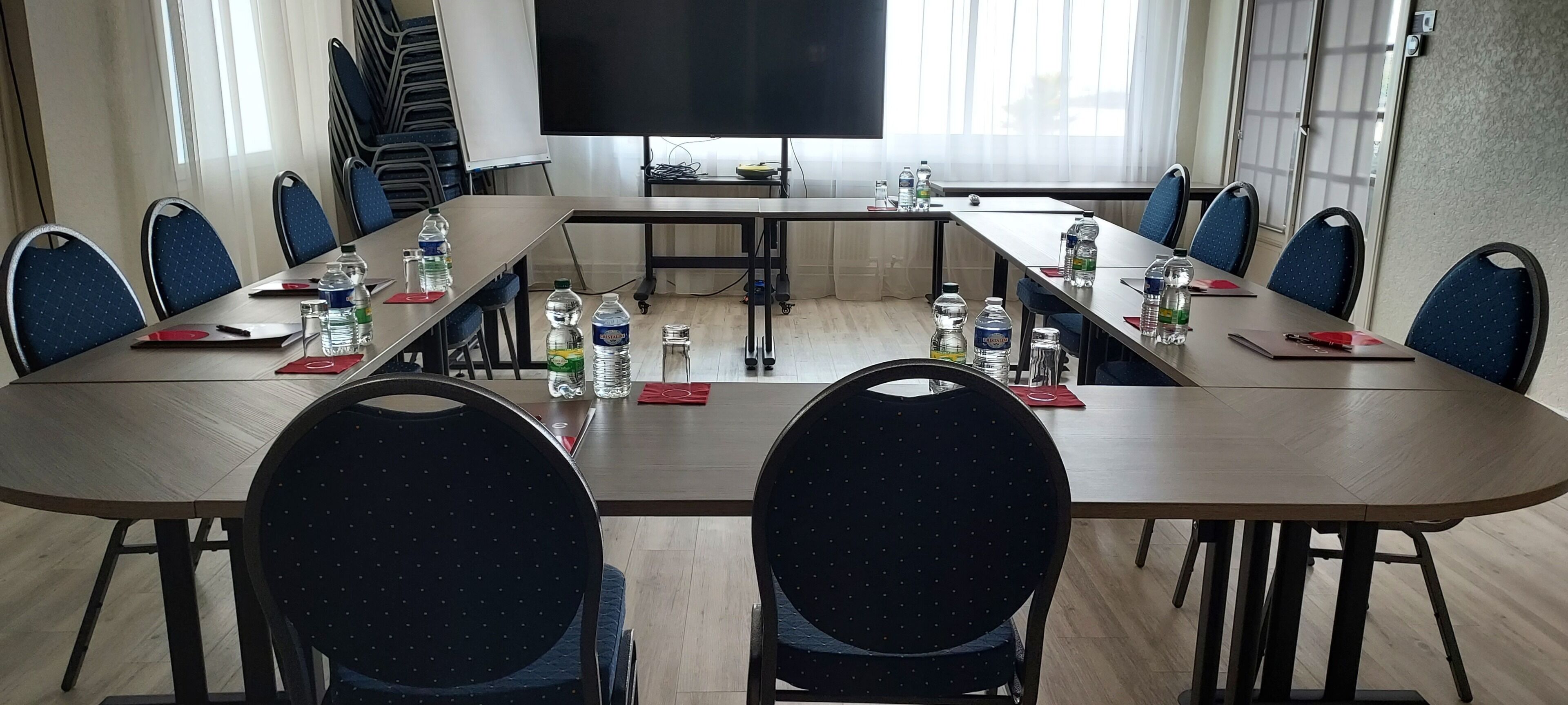 A conference room with a long table, chairs, water bottles, and a TV screen.
