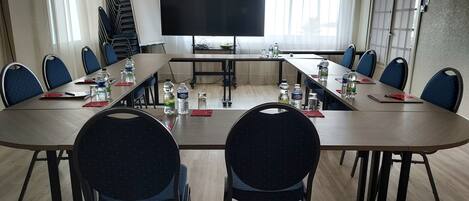 A conference room with a long table, chairs, water bottles, and a TV screen.