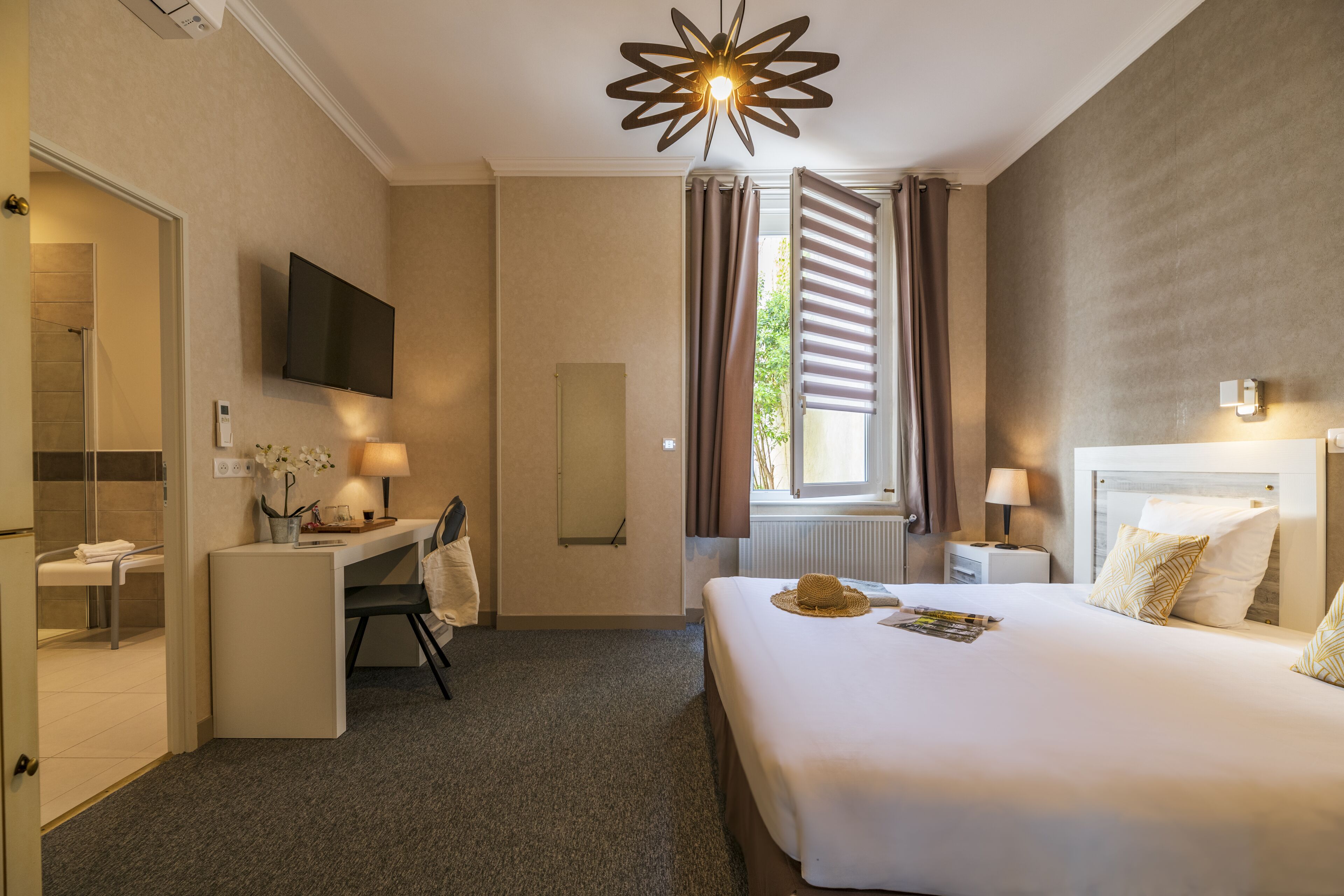 Una habitación de hotel con cama, escritorio, silla, televisor y ventana con cortinas.