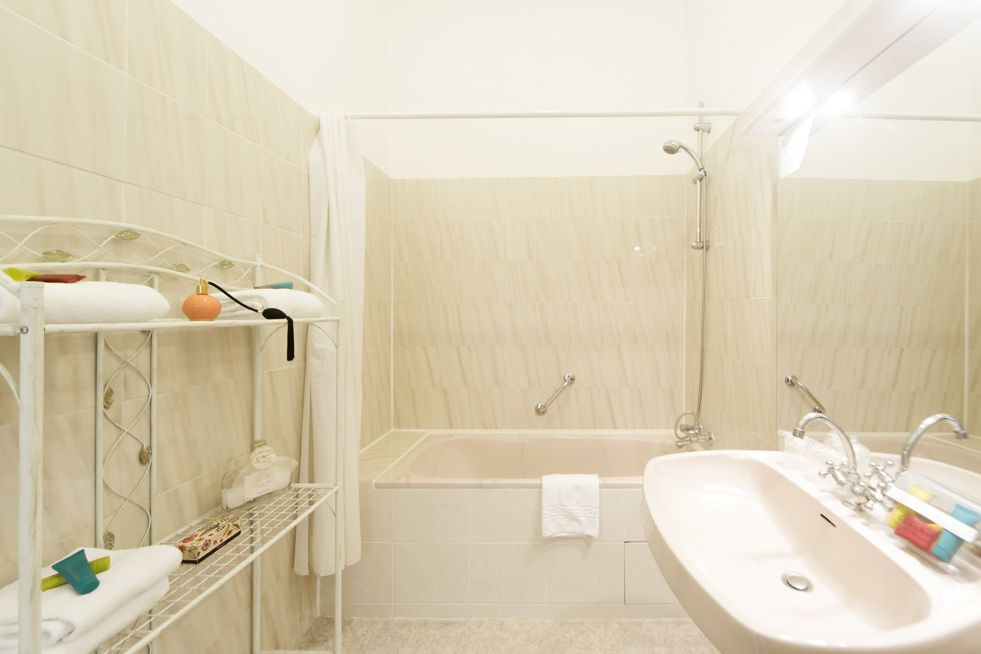 A bathroom with a bathtub, a sink, and a shower. There are towels and toiletries on shelves.