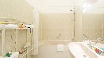 A bathroom with a bathtub, a sink, and a shower. There are towels and toiletries on shelves.