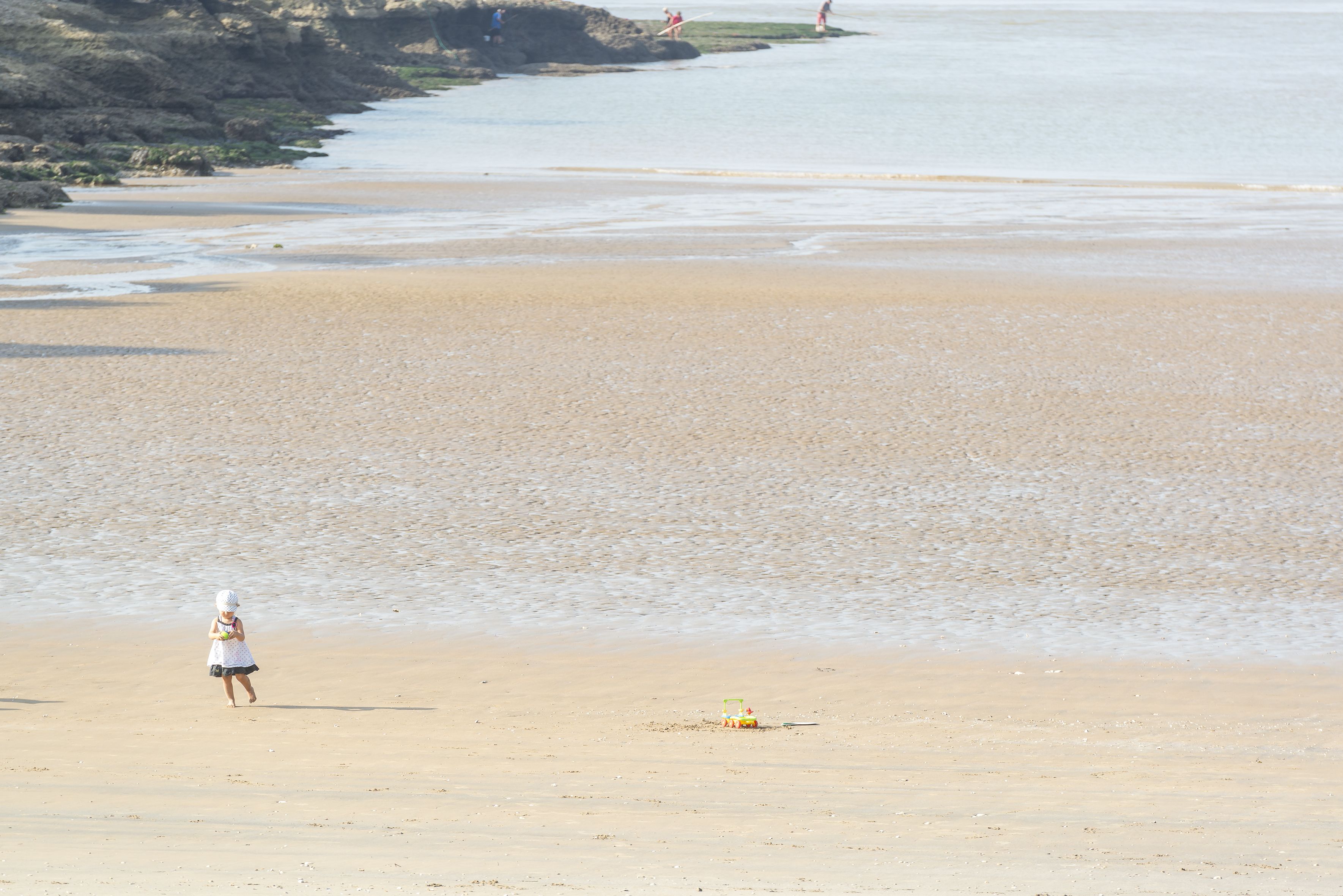 A beach with a person walking, a lifeguard tower, and a rocky coastline.