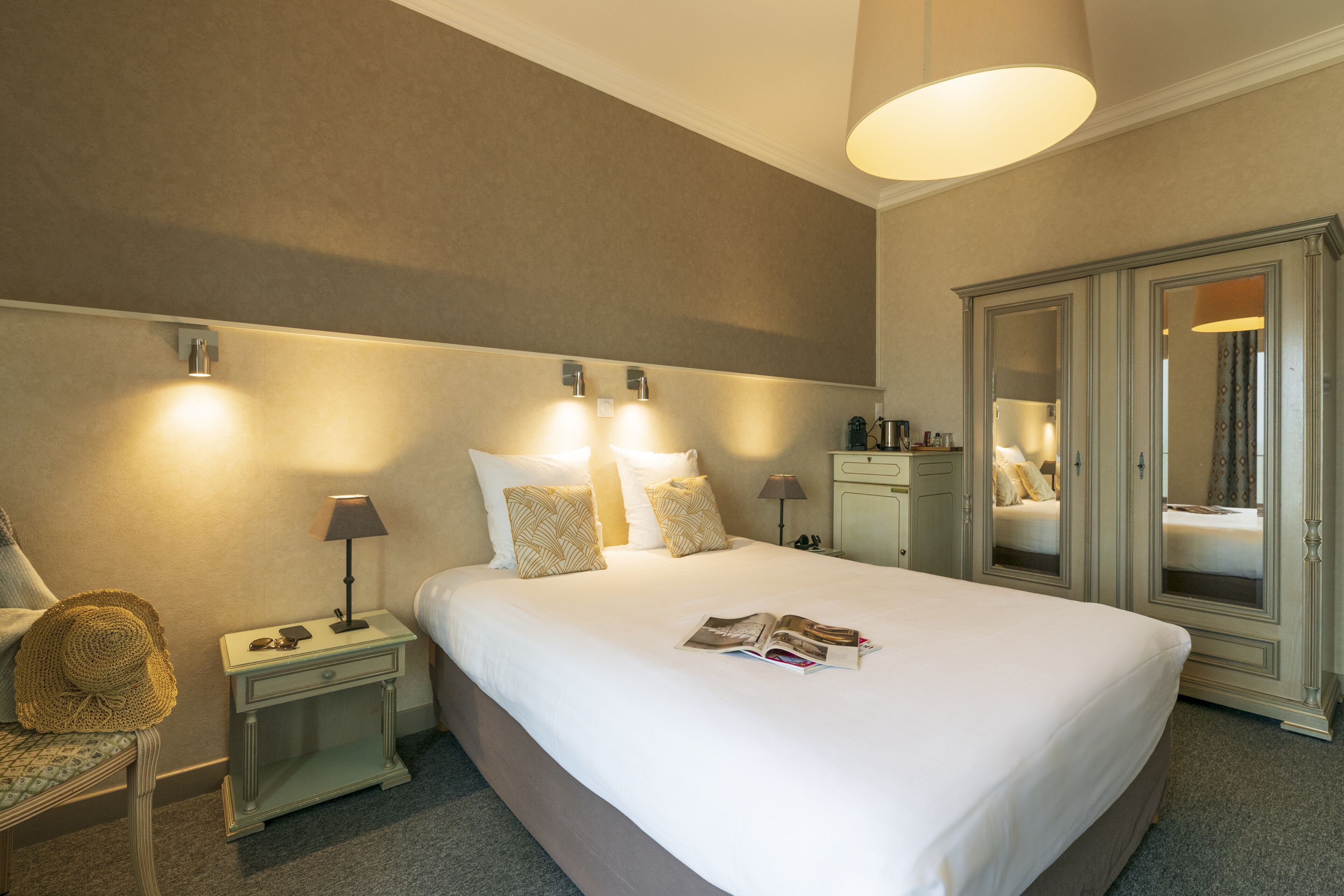 Ein ordentlich eingerichtetes Hotelzimmer mit einem großen Bett, Nachttischlampen, einem Nachttisch, einem Sessel und einem Kleiderschrank.