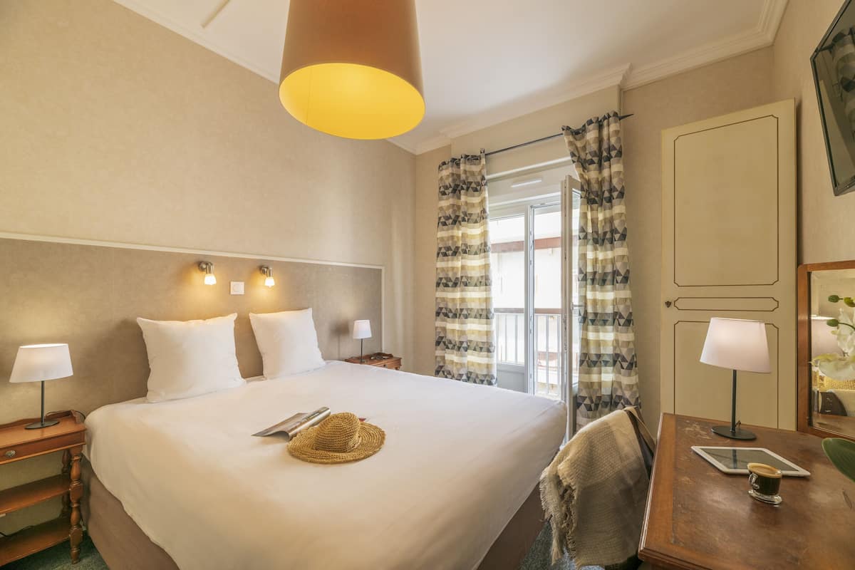 A hotel room with a large bed, bedside lamps, a wooden desk, a tablet, and a coffee cup.