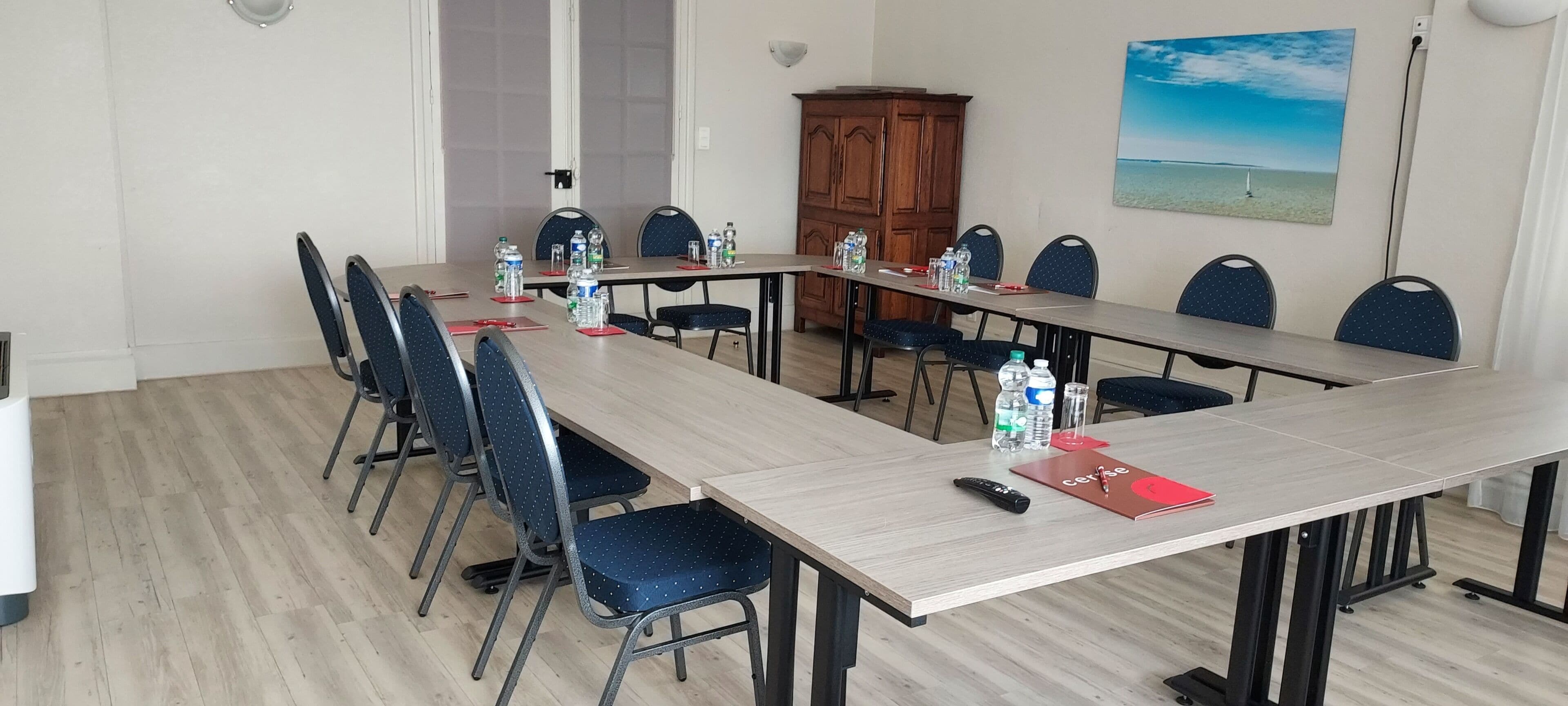 Ett konferensrum med ett långt bord, stolar, vattenflaskor och en röd pärm på bordet.