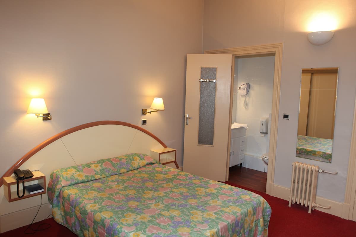 A bedroom with a bed, bedside lamps, a telephone, a radiator, and a bathroom door.
