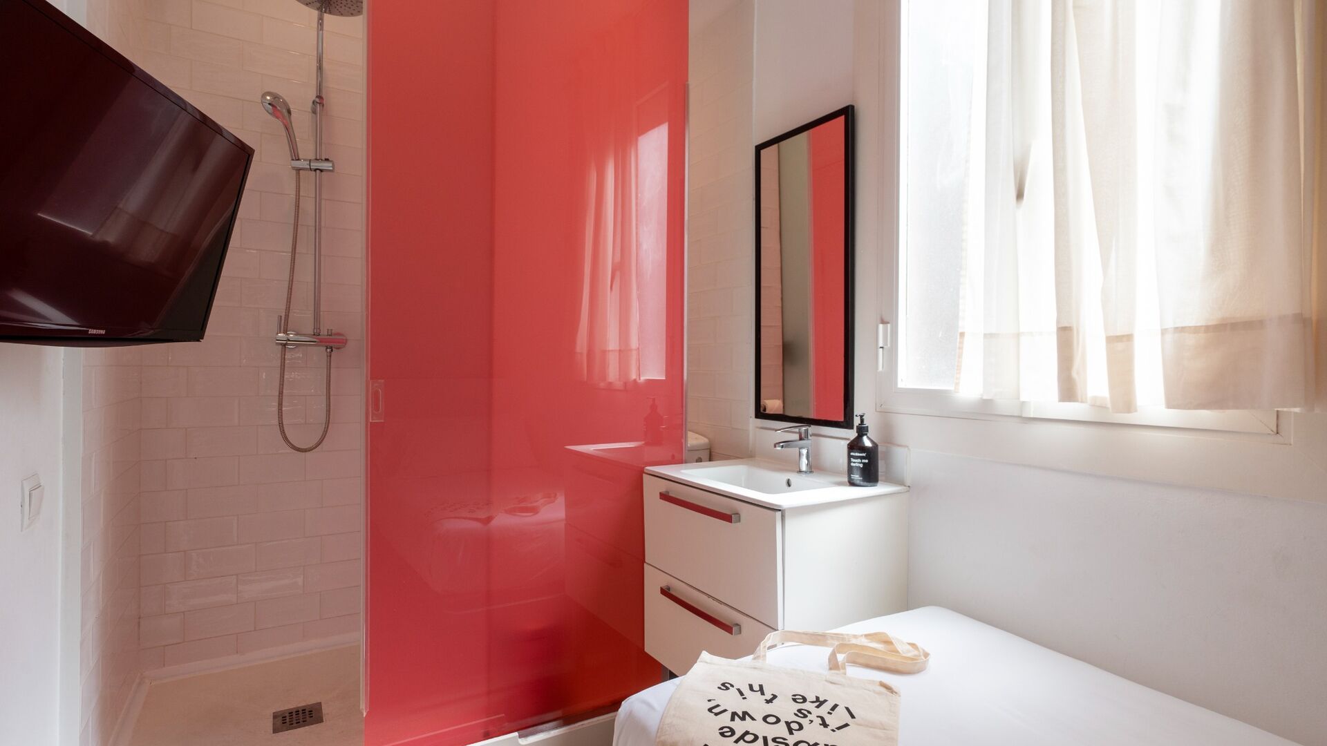 A bathroom with a shower, a sink, a mirror, and a window with curtains.