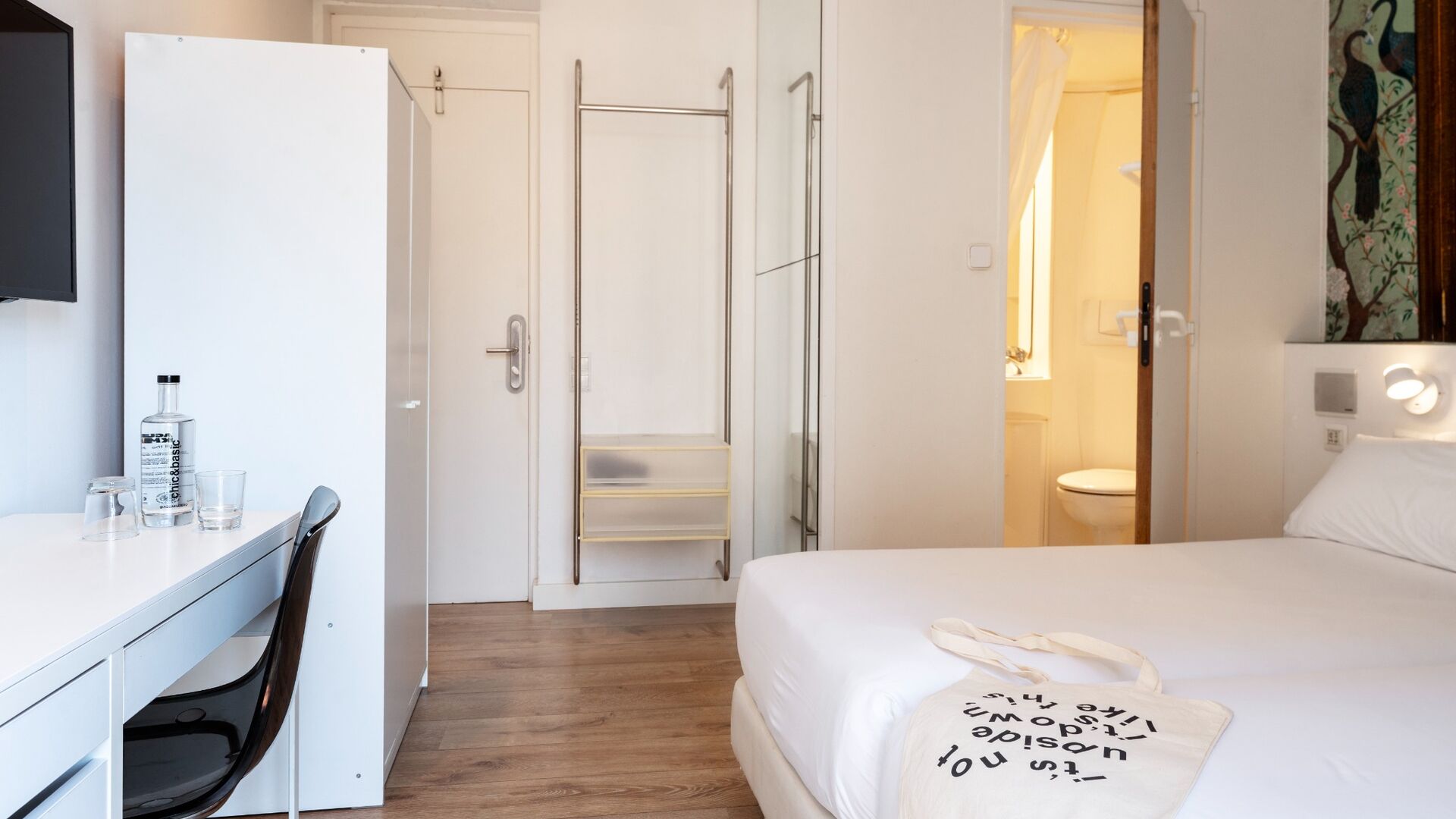Habitació d'hotel amb un llit, escriptori amb cadira, armari i bany visible per una porta oberta.