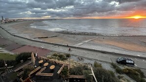 A coastal road with a beach, a restaurant with outdoor seating, and a sunset in the background.