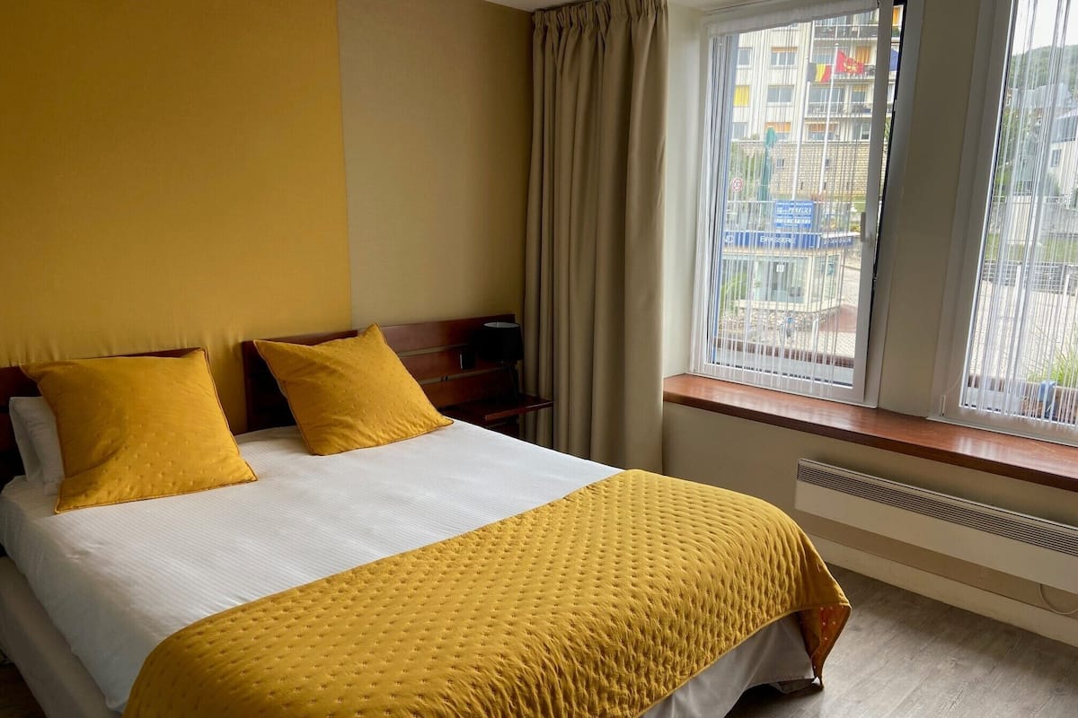 Una habitación de hotel con cama, dos almohadas, ventana con cortinas y radiador.