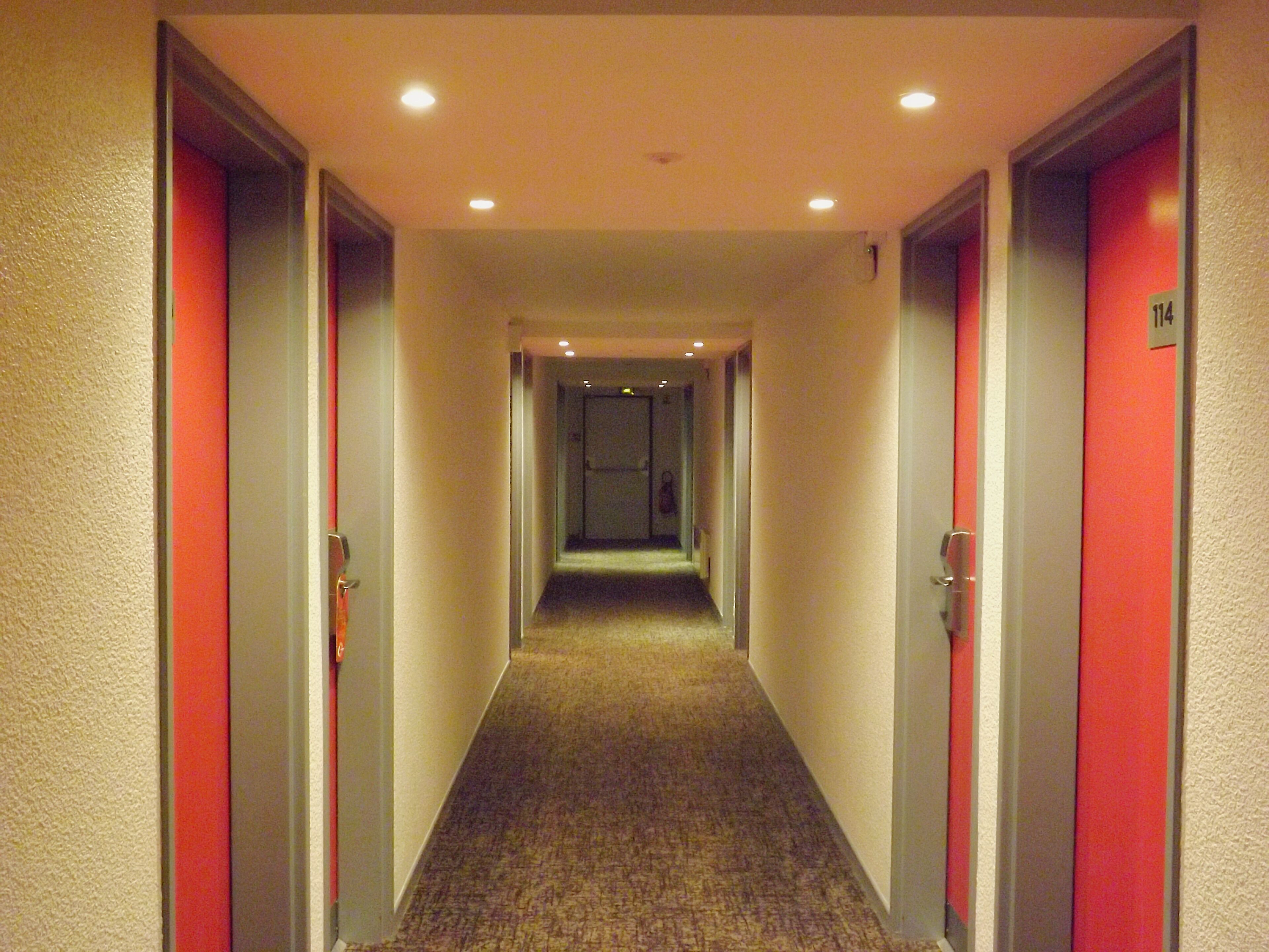 A hotel hallway with carpeted floors, doors on both sides, and a number sign on the right wall.