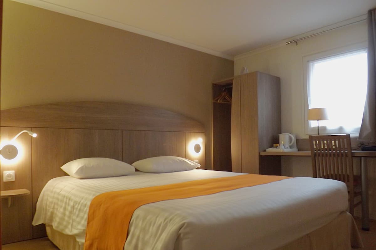 Une chambre d’hôtel avec un lit, des lampes de chevet, un bureau avec une chaise et une fenêtre.