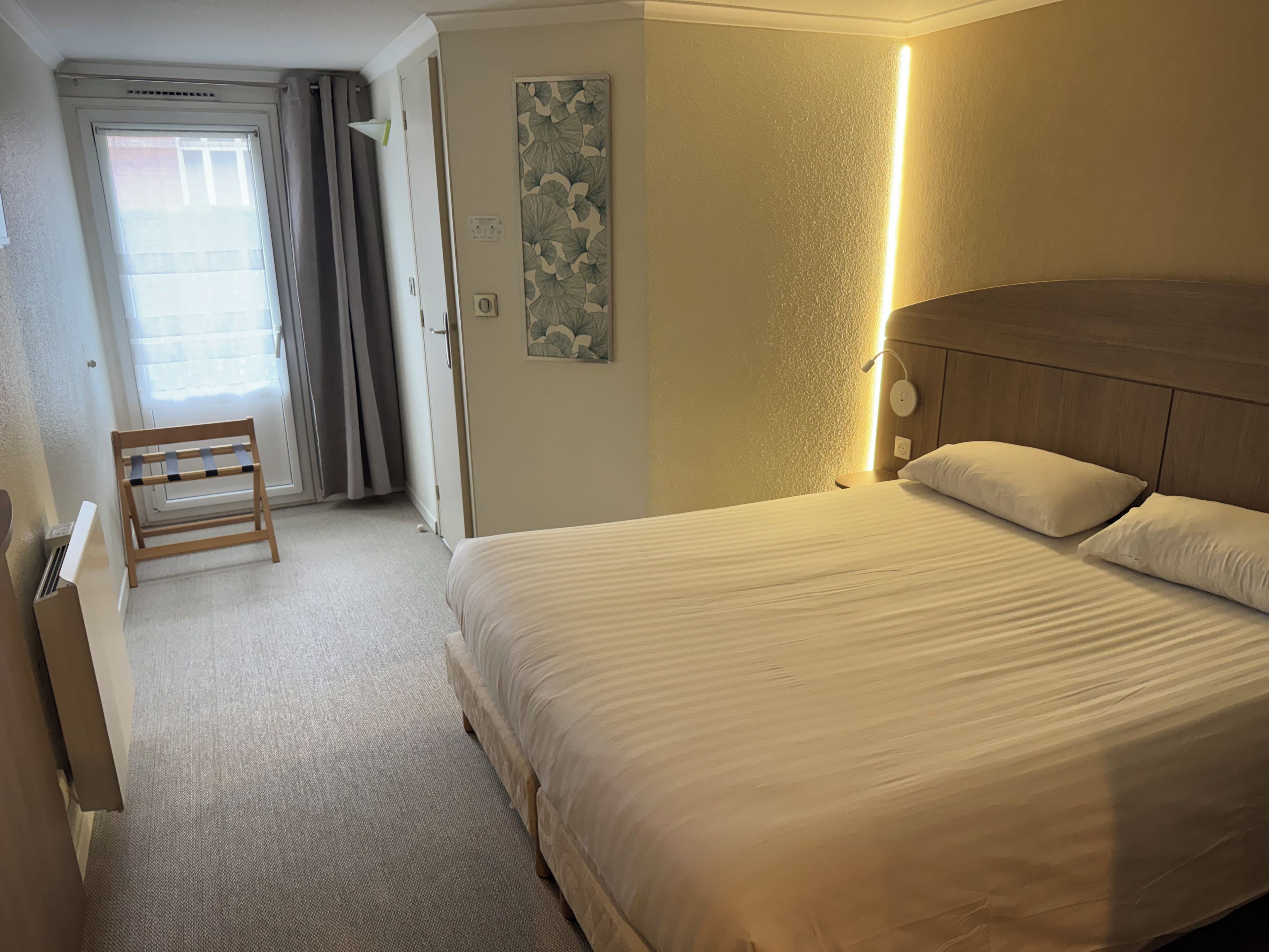 A hotel room with a bed, a bedside table, a lamp, a chair, and a door leading to a balcony.
