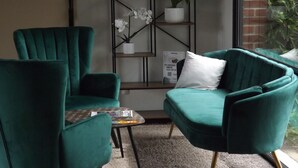 A teal armchair and sofa set, a small table with a magazine, a potted orchid, and a bookshelf with books and a plant. - The Originals City, Hôtel Le Gayant (Douai)