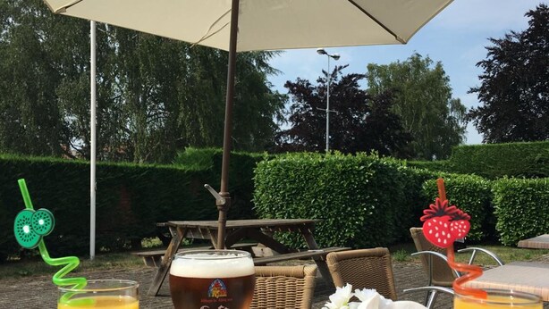 An outdoor dining area with a table set for two, featuring a glass of beer, two fruit juices, a bowl of nuts, and a metal cup. - The Originals City, Hôtel Le Gayant (Douai)