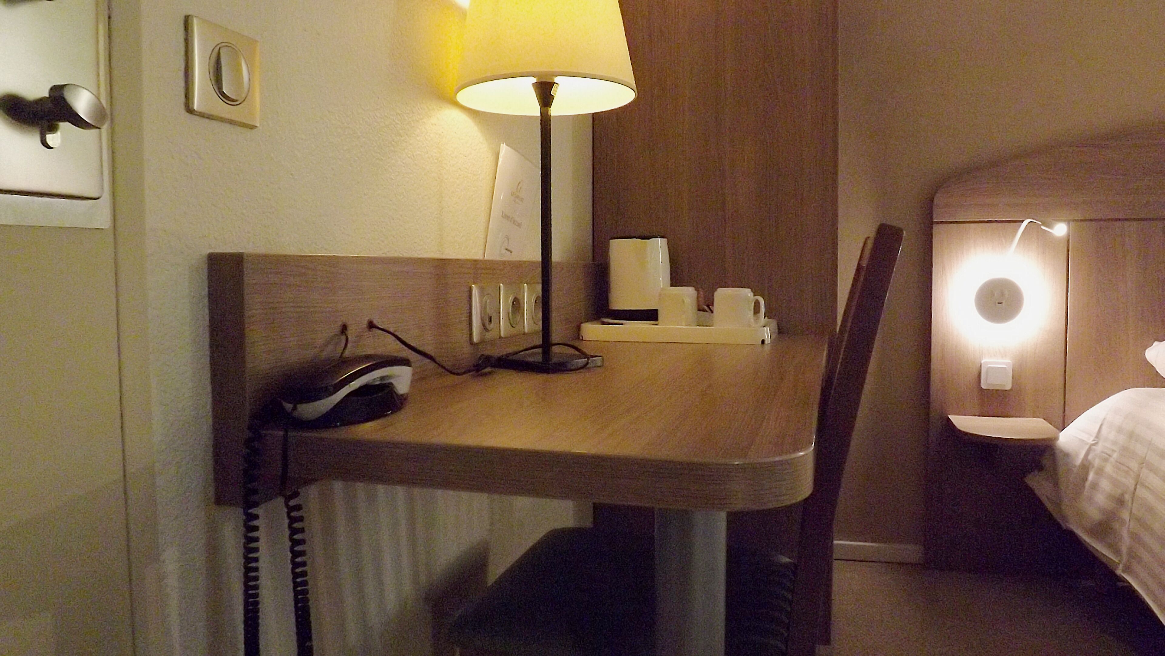 Une chambre d’hôtel équipée d’un bureau, d’une lampe, d’un téléphone et d’un lit.