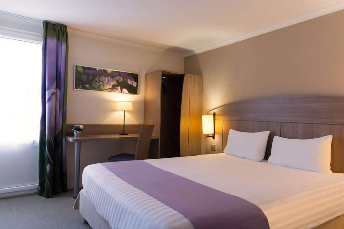 Une chambre d’hôtel avec un grand lit, un bureau avec une chaise, une lampe et un tableau au mur.