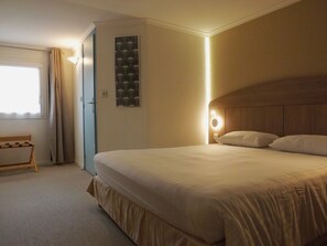 Una habitación de hotel con cama, mesita de noche, lámpara de pared y una puerta.