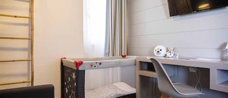 Una cuna para bebé con dosel estampado de estrellas, un escritorio pequeño con una silla y un televisor instalado en la pared.
