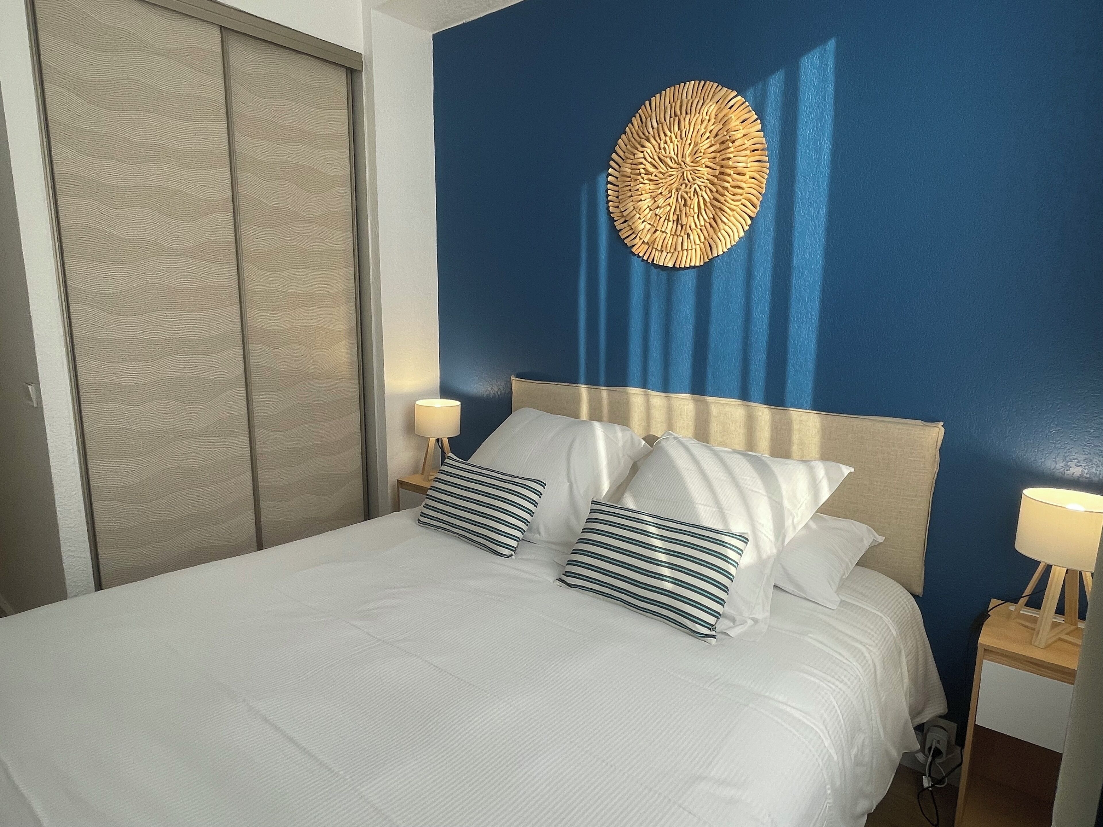A hotel room with a bed, two bedside lamps, a wall-mounted decorative item, and a wardrobe.