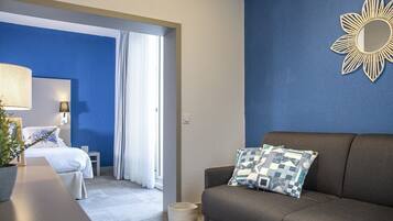 Habitación de hotel con cama, sofá, espejo decorativo y una pared de acento azul.