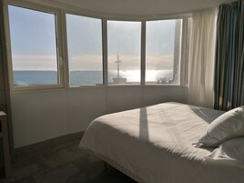 Un dormitorio con un ventanal que ofrece vistas al mar y una torre distante.