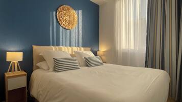 Una cama con ropa de cama blanca, dos lámparas de noche y un adorno en la pared.
