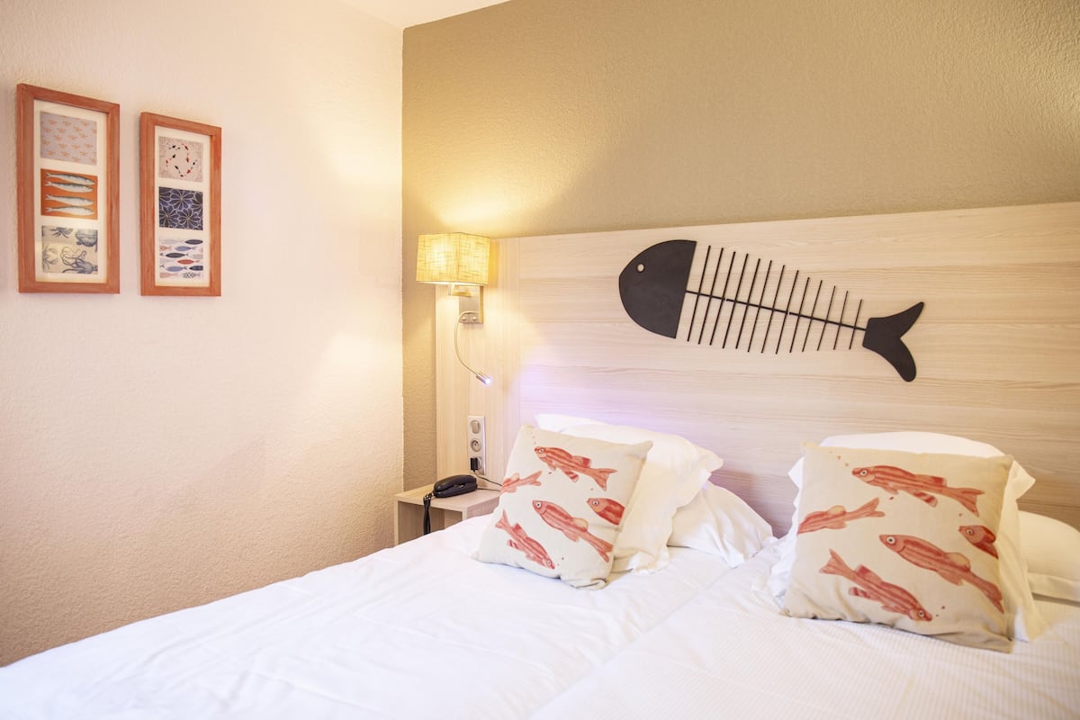 Quarto de hotel com uma cama, duas almofadas com estampas de peixe, um enfeite de peixe na parede e duas quadros emoldurados.
