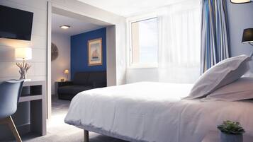 Une chambre d’hôtel avec un lit, un bureau, une chaise, une télévision, une fenêtre avec des rideaux et une petite plante.