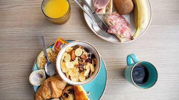A breakfast setting with a plate of croissants, a bowl of cereal, a glass of orange juice, a plate with ham, kiwi, and a banana.