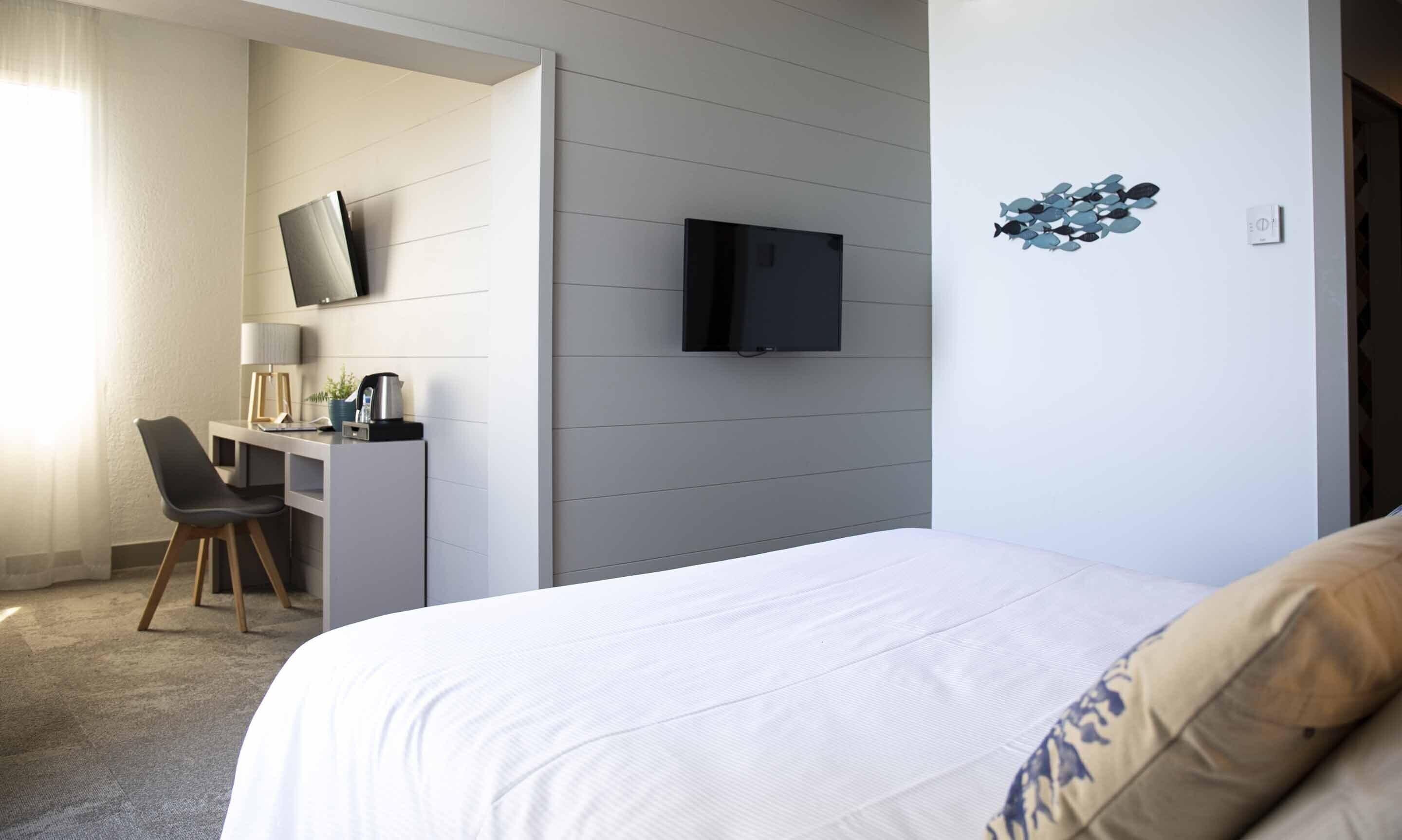 Ein Hotelzimmer mit einem Bett, einem Schreibtisch mit Stuhl, einem Fernseher und einem Wandbild.