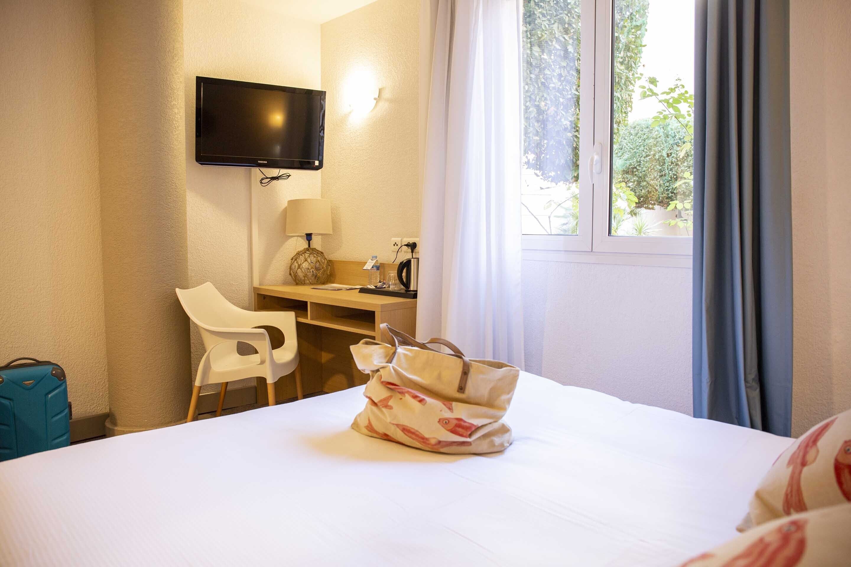 A hotel room with a bed, a desk, a chair, a television, and a window with curtains.