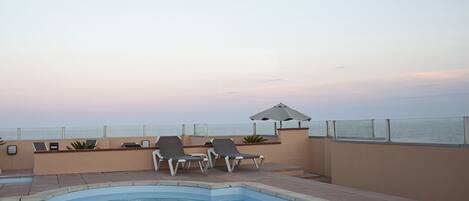 Una piscina con sillas de descanso y vista al océano.