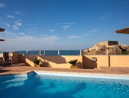 Piscina con vistas al océano, rodeada de sillas de descanso y sombrillas.