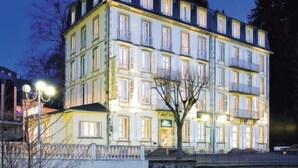 A multi-story hotel with balconies, a stone facade, and a reflection in the water. - Le Parc des Fées (La Bourboule)