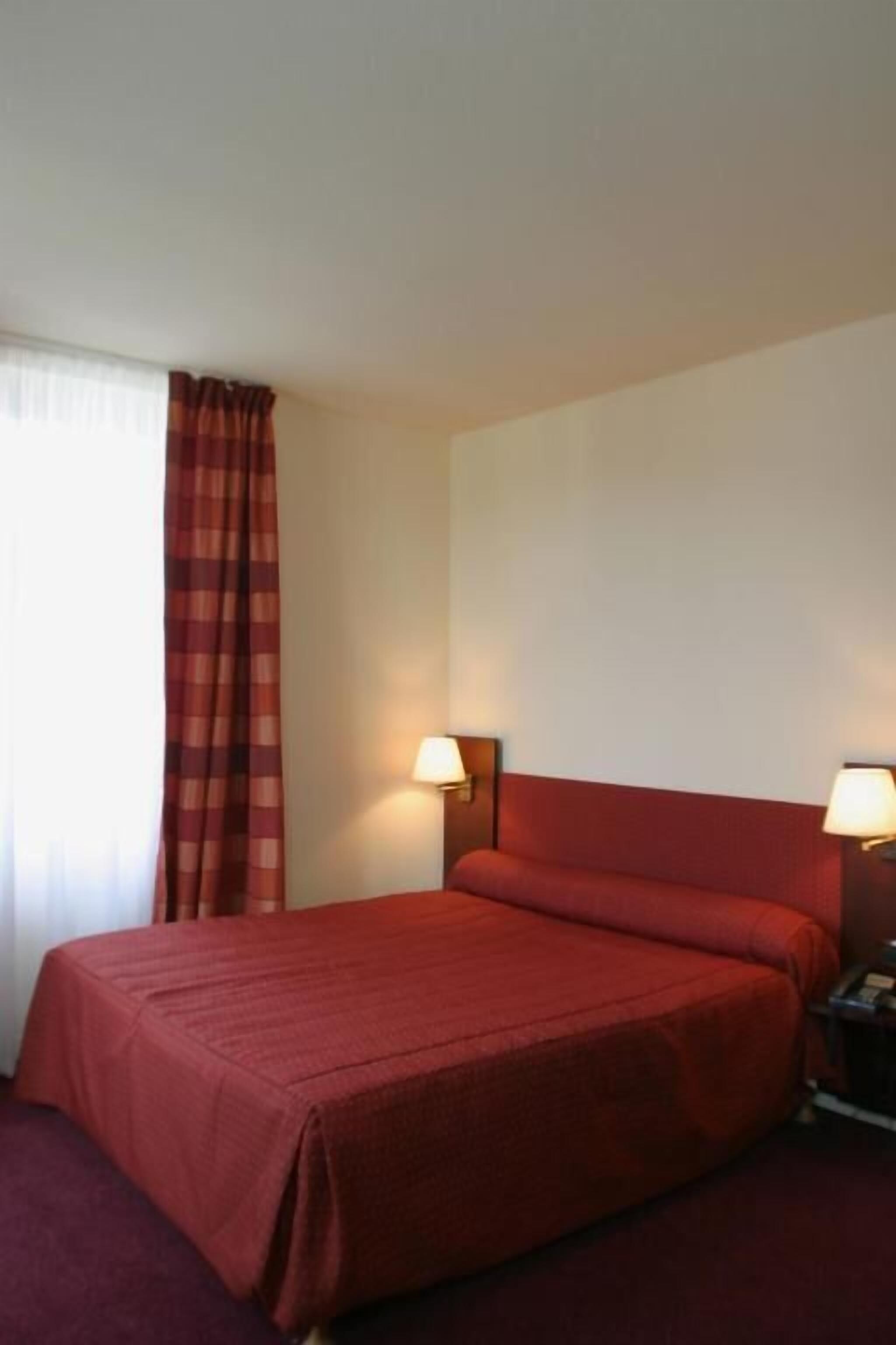 Een hotelkamer met een groot bed, twee bedlampjes, een rood hoofdeinde en een raam met een rode gordijn.