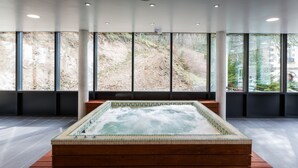 A modern spa area with a hot tub, large windows, and a view of a hillside. - Le Parc des Fées (La Bourboule)