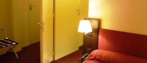 A hotel room with a bed, a nightstand, a lamp, and a door leading to another room.