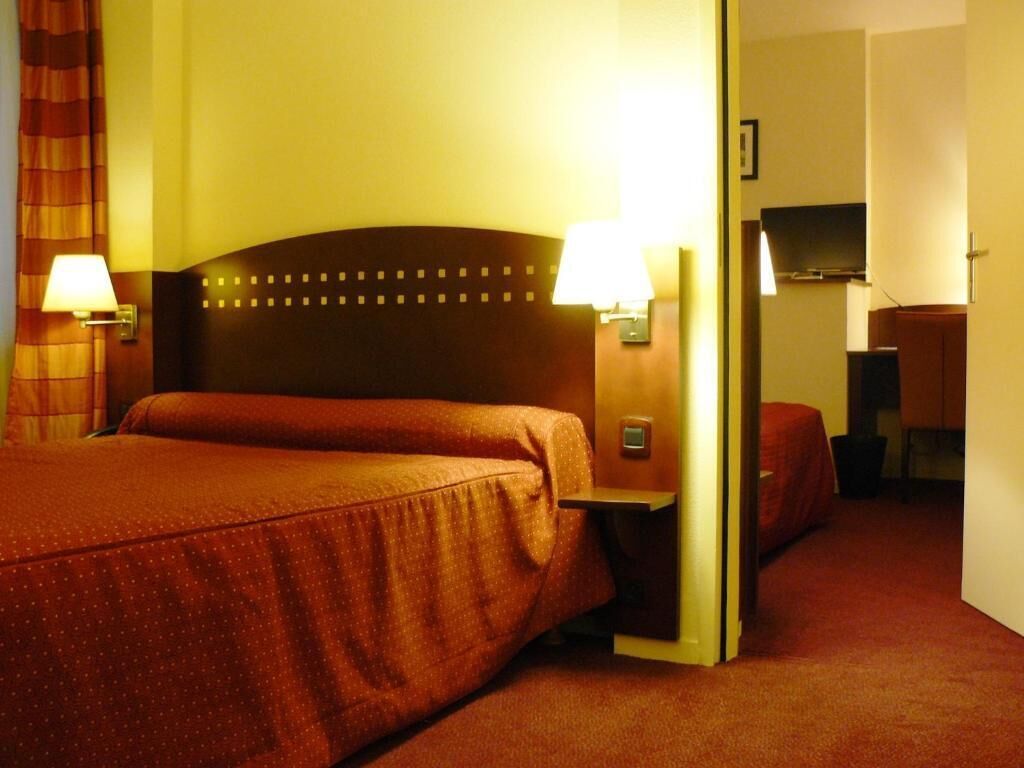 Ein Hotelzimmer mit einem großen Bett, zwei Nachttischlampen, einem Flachbildfernseher und einer Tür zu einem weiteren Raum.